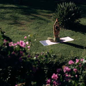 Person practicing yoga on a mat in a garden with flowers and plants.