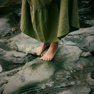 Person wearing a green dress standing on rocks by a stream
